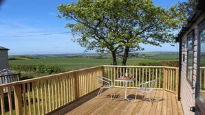Een houten terras met een tafel en stoelen, met uitzicht op een groen landschap.
