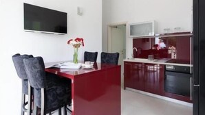 Cocina moderna con una isla roja, paredes blancas y un televisor de pantalla plana montado sobre la isla.