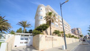 A multi-story hotel with a stone facade, palm trees, and a clear blue sky. - Apto CasaTuris 1Línea Muchavista C101 (Ibi)