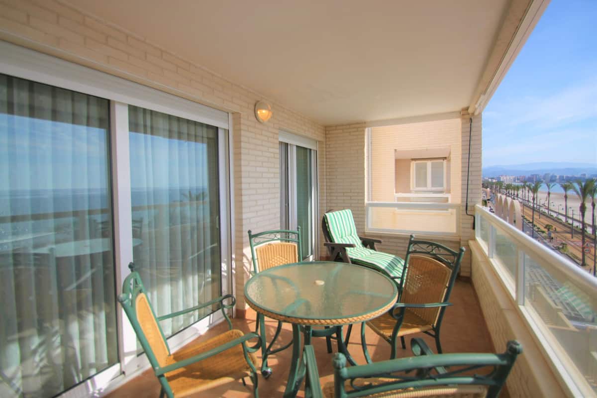 Un balcon avec une table et des chaises en verre, une vue sur le paysage urbain et un mur de briques.