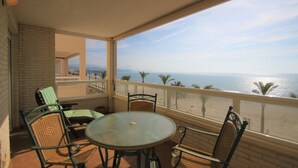 A balcony with a round table and chairs, overlooking a beach and ocean. - Apto CasaTuris 1Línea Muchavista C101 (Ibi)
