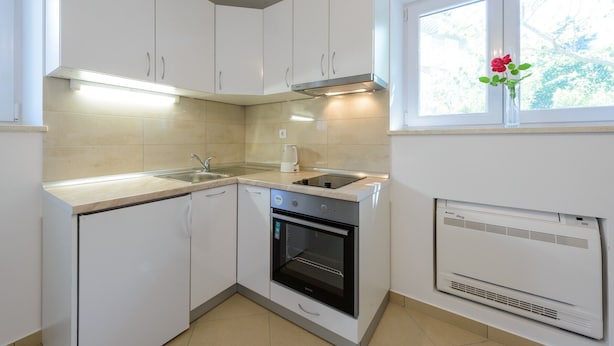 Una cocina moderna con armarios blancos, horno integrado, lavamanos y ventana con un jarrón de flores.