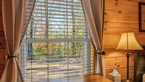 Una habitación con detalles de madera, una ventana con persianas, una mesa con caja de pañuelos y una lámpara.