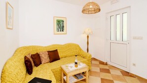 Ett rum med en gul, mönstrad soffa, ett litet träbord med en flaska och glas på, en lampa och en dörr med tre fönster.