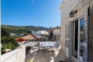 Un balcon avec une table et des chaises, un pot de fleurs et une vue sur une colline et des bâtiments.