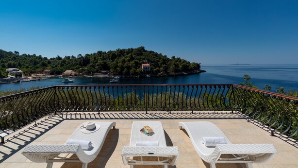 A terrace with white wicker lounge chairs and a table, overlooking a body of water and a forested island. - Villa Amfora- Six Bedroom Villa with Terrace and Swimming Pool, 2X Jacuzzi and Sea View (Prižba)
