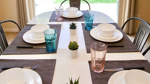 Una mesa de comedor con platos, fuentes, vasos y cubiertos, con vistas a la vegetación exterior.