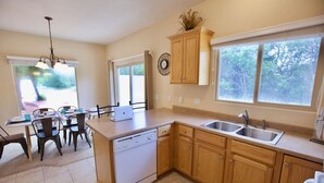 Una cocina con armarios de madera, lavavajillas, fregadero y comedor con sillas y mesa.