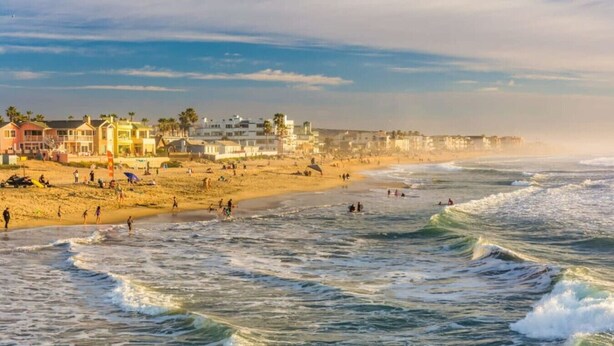 A beach with waves, people, and buildings in the background.