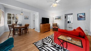 A spacious living area with a dining table, a red sofa, a TV, and a ceiling fan. - Ben`s Beach Bungalow 2, 100 Steps to Sand (San Diego)