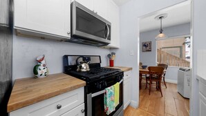 A compact kitchen with a stove, microwave, and a dining area with a table and chairs. - Ben`s Beach Bungalow 2, 100 Steps to Sand (San Diego)