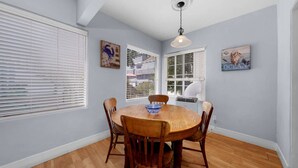 A dining room with a wooden table, four chairs, a blue bowl, and artwork on the walls. - Ben`s Beach Bungalow 2, 100 Steps to Sand (San Diego)