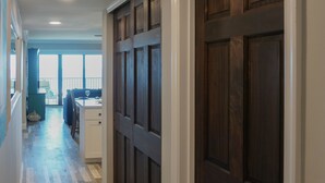 Un pasillo con piso de madera, una puerta de madera oscura y un ventanal al final.