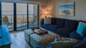 Un salón con un sofá azul, un reposapiés estampado y vistas a la playa a través de un ventanal corredero.