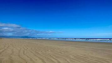 Een breed zandstrand met zachte golven en een helderblauwe lucht.