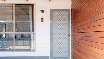 A building with a white exterior, a wooden door with a metal grid, and a window with a patterned blind.