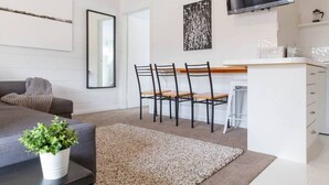 A modern living room with a grey sofa, a coffee table with a plant, a dining area with chairs and a table, and a kitchen area with a TV. - Prom Coast 2~Getaway to Wilson`s Prom. Walk 2Beach (Sandy Point)