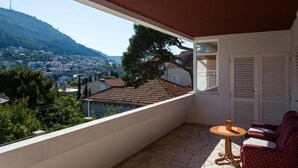Un balcon donnant sur une ville située sur une colline, une table avec une chaise et une porte avec des volets.