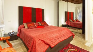 A bedroom with a large bed, a wooden headboard, a nightstand, a mirror, and a chair. - Venice Dream House Figaro (Venice)