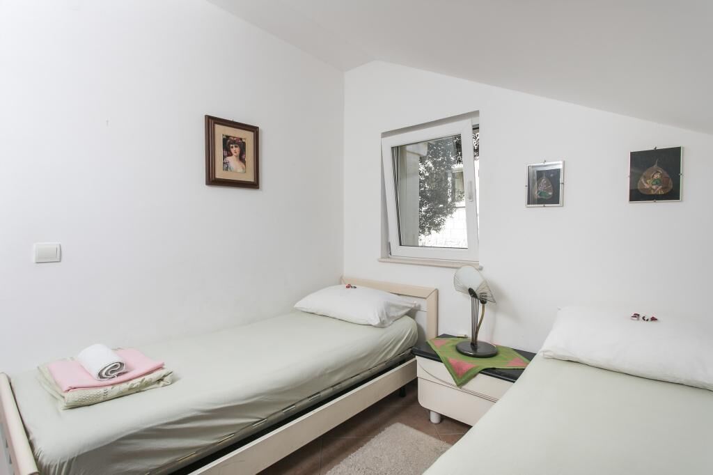 A small, clean room with two single beds, a window, and a few wall-mounted pictures.
