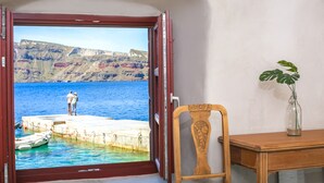 A room with a view of a pier and cliffs, a wooden chair, and a vase with a plant. - Seafront Cave Suite (Santorini)