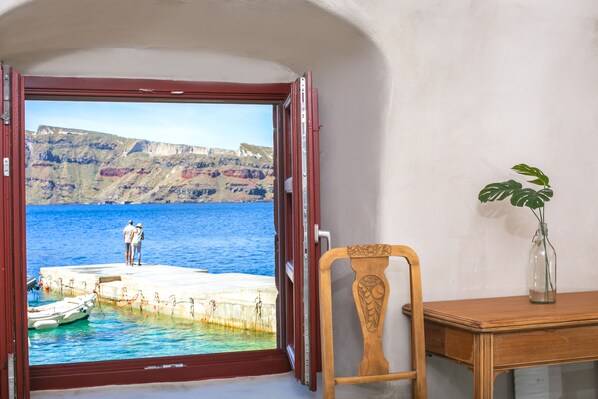 Quarto com vista para um cais e falésias, uma cadeira de madeira e um vaso com uma planta.