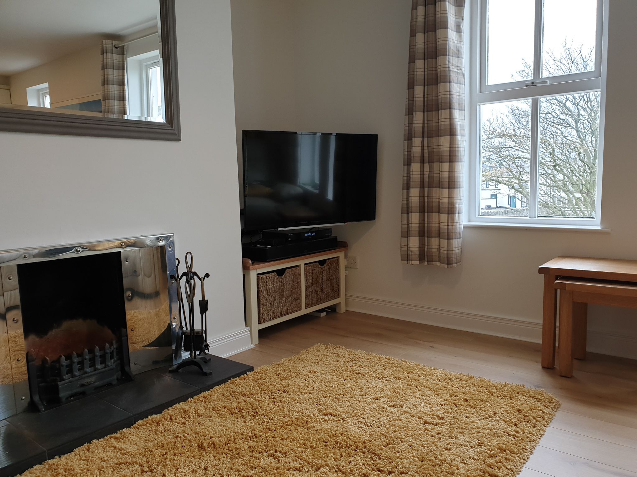 A living room with a fireplace, a flat-screen TV, a large window with curtains, and a wooden table.