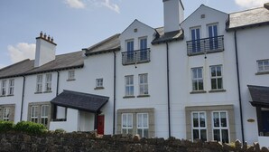 A row of white townhouses with stone walls, multiple windows, and a red door. - Coastal View (Bushmills)