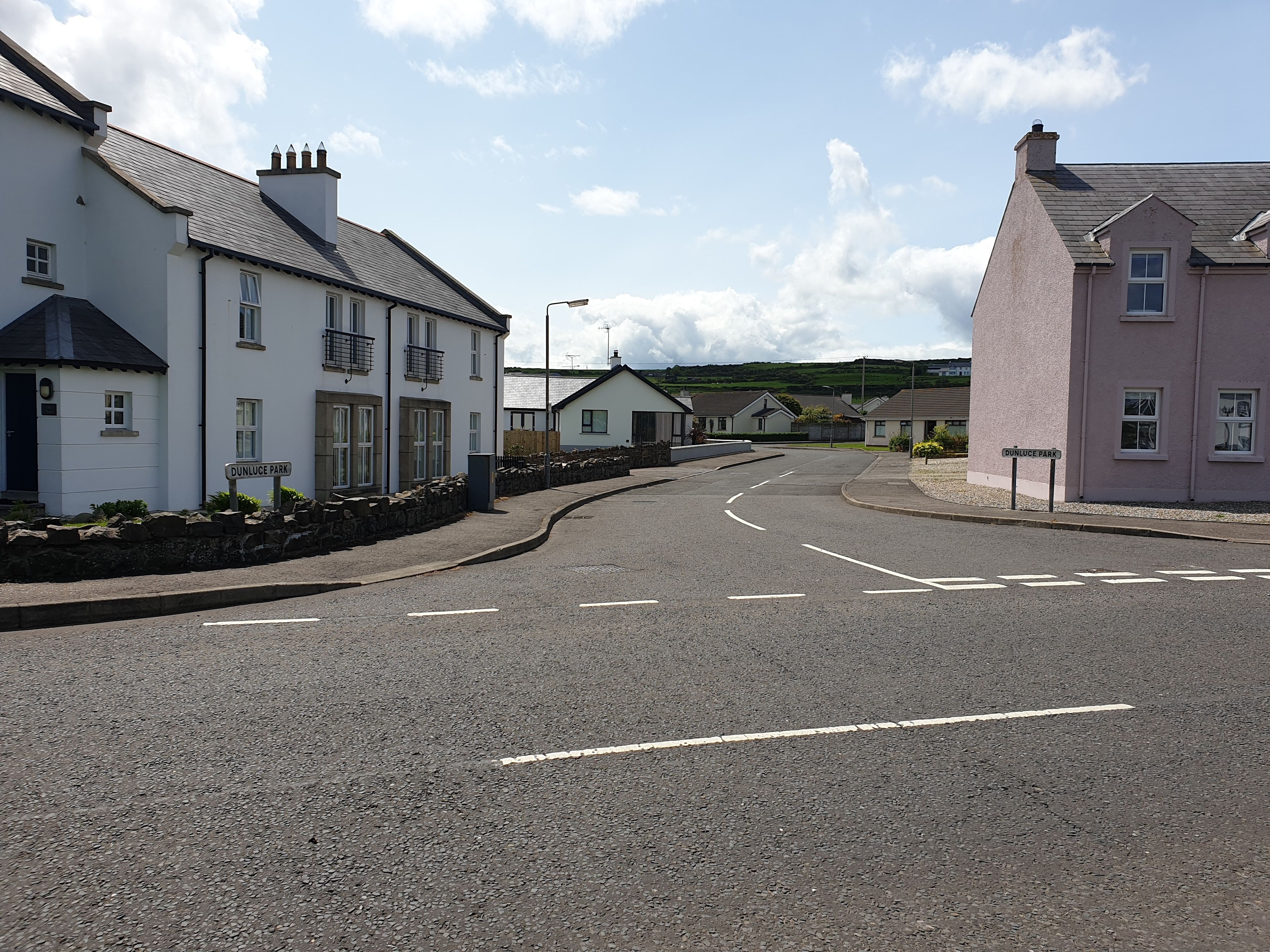 A residential street with houses, a clear sky, and a road marked with white lines.