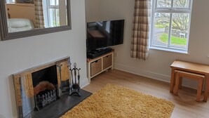 A living room with a fireplace, a television, a window with curtains, and a wooden bench. - Coastal View (Bushmills)