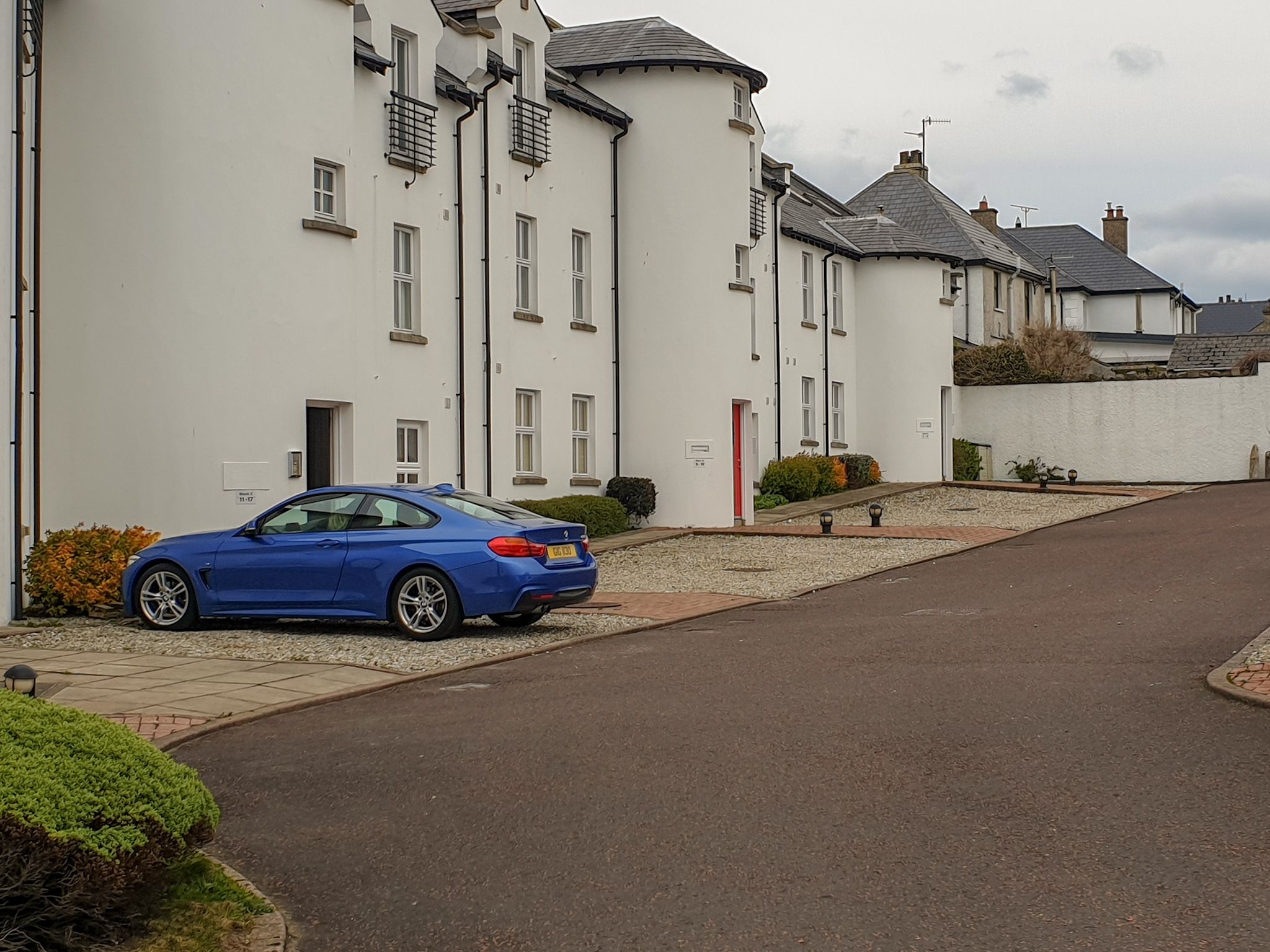 Una calle residencial con un coche azul estacionado frente a una casa blanca.