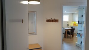 A hallway leading to a dining area with a wooden table and chairs, a hanging light fixture, and a coat rack with hooks. - Coastal View (Bushmills)