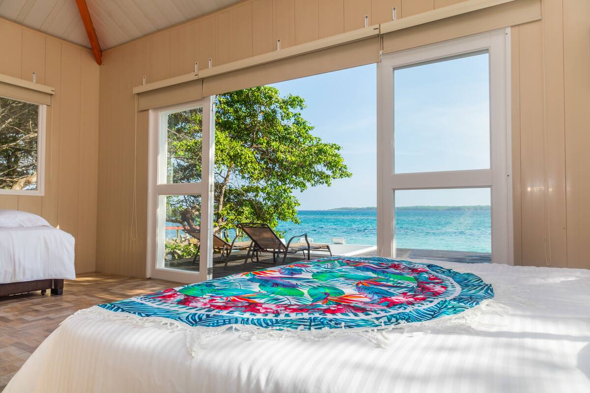 Een slaapkamer met een bed, uitzicht op de oceaan en een boom voor het raam.