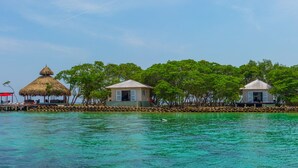 Une petite île dotée de trois constructions à toits de chaume et d’une jetée en bois qui s’avance dans des eaux turquoise.