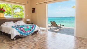 Une chambre avec un lit, une fenêtre donnant sur l’océan et un balcon avec une chaise.