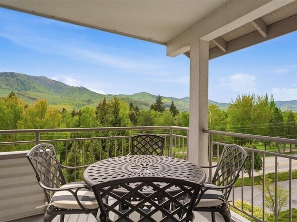 A balcony with a table and chairs, overlooking a mountainous landscape.