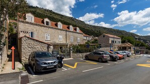 Ein Parkplatz mit Autos und ein Steinhaus mit vielen Fenstern und einem roten Ziegeldach.