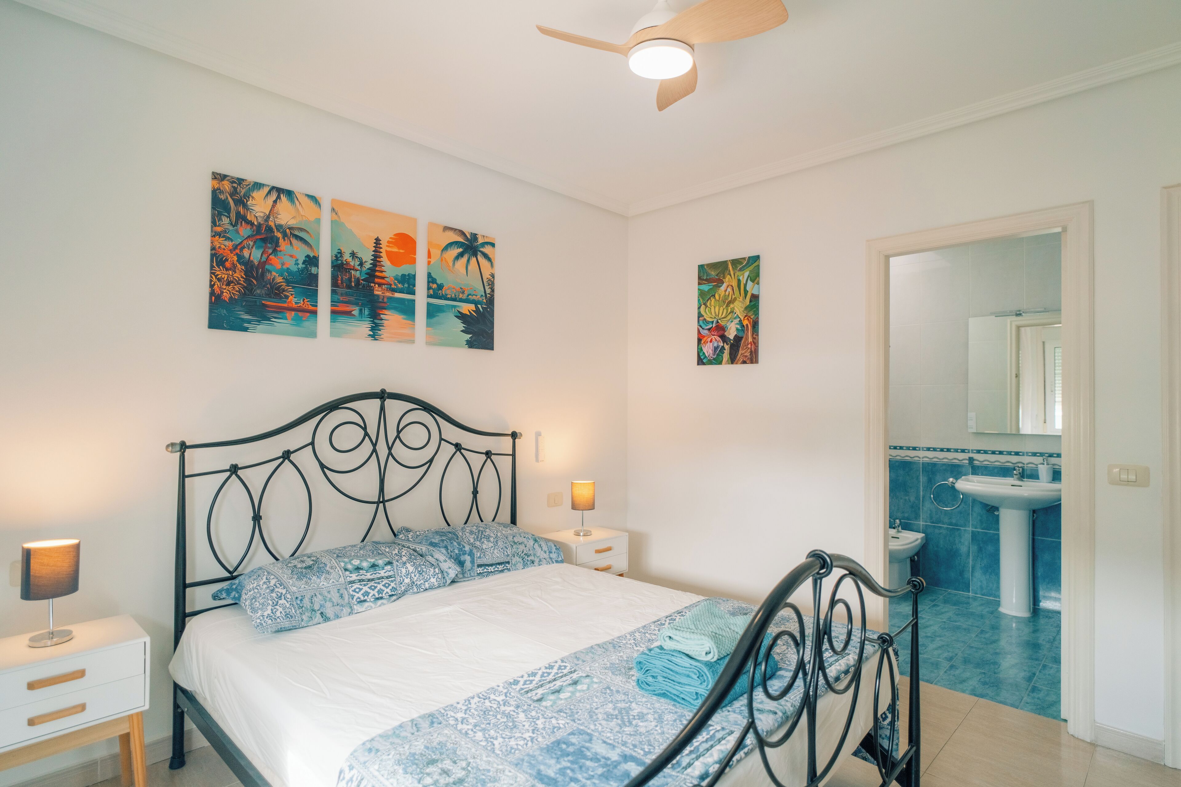 A bedroom with a bed, nightstands, a ceiling fan, and artwork on the wall.