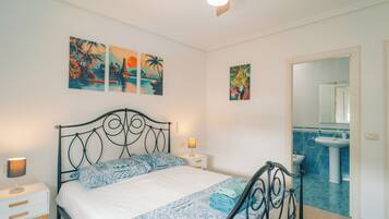 A bedroom with a bed, nightstands, a ceiling fan, and artwork on the wall.