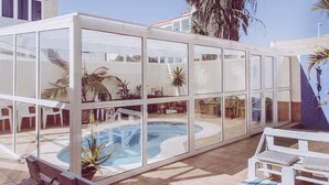 A glass-enclosed pool area with a bench and chairs, surrounded by potted plants. - Aloe Vera Shared House - Hostel (Granadilla de Abona)