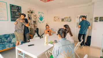 Una habitación con una mesa blanca, sillas y un sofá. Hay gente sentada y de pie alrededor.