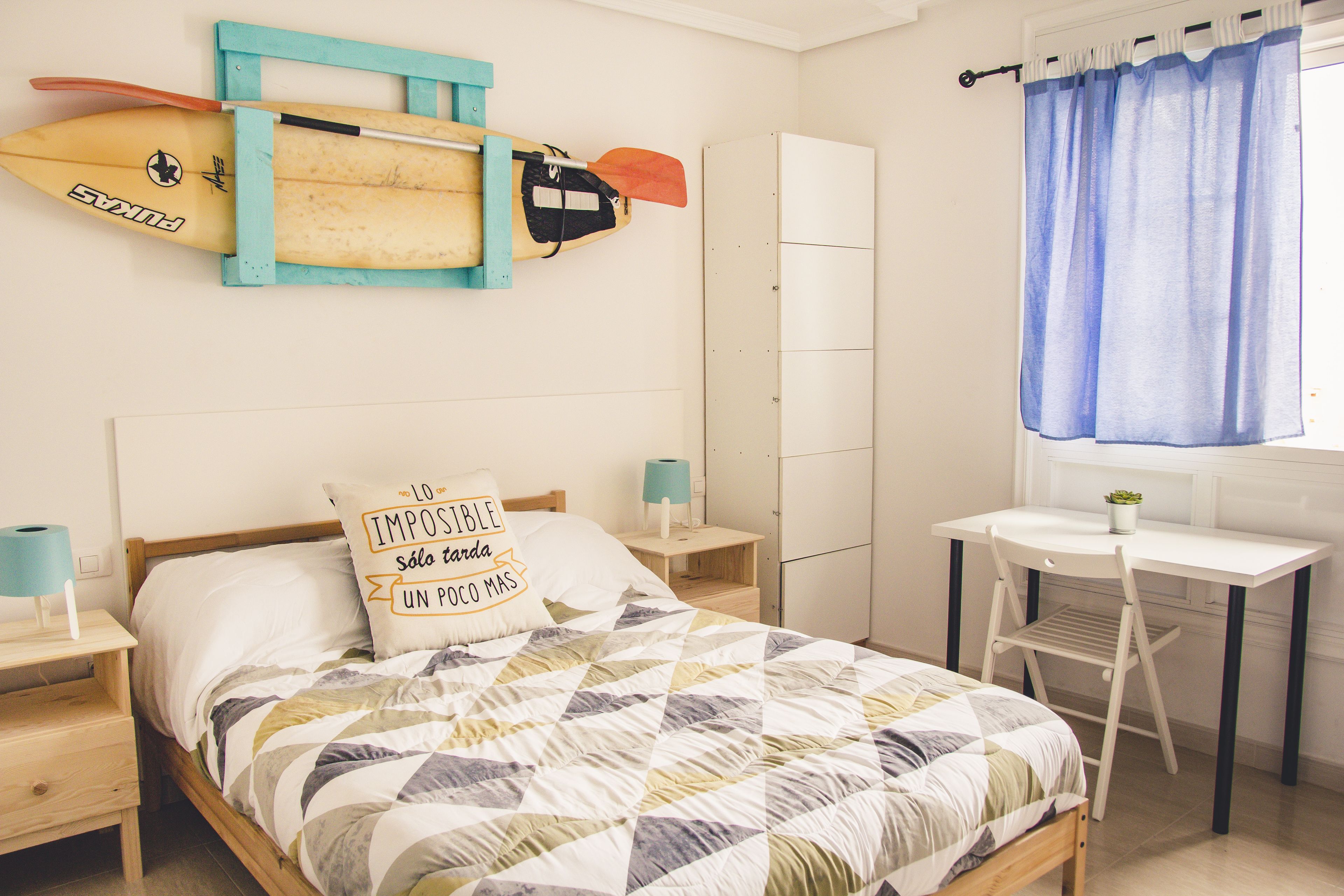 Une chambre avec un lit, un bureau et deux planches de surf accrochées au mur.