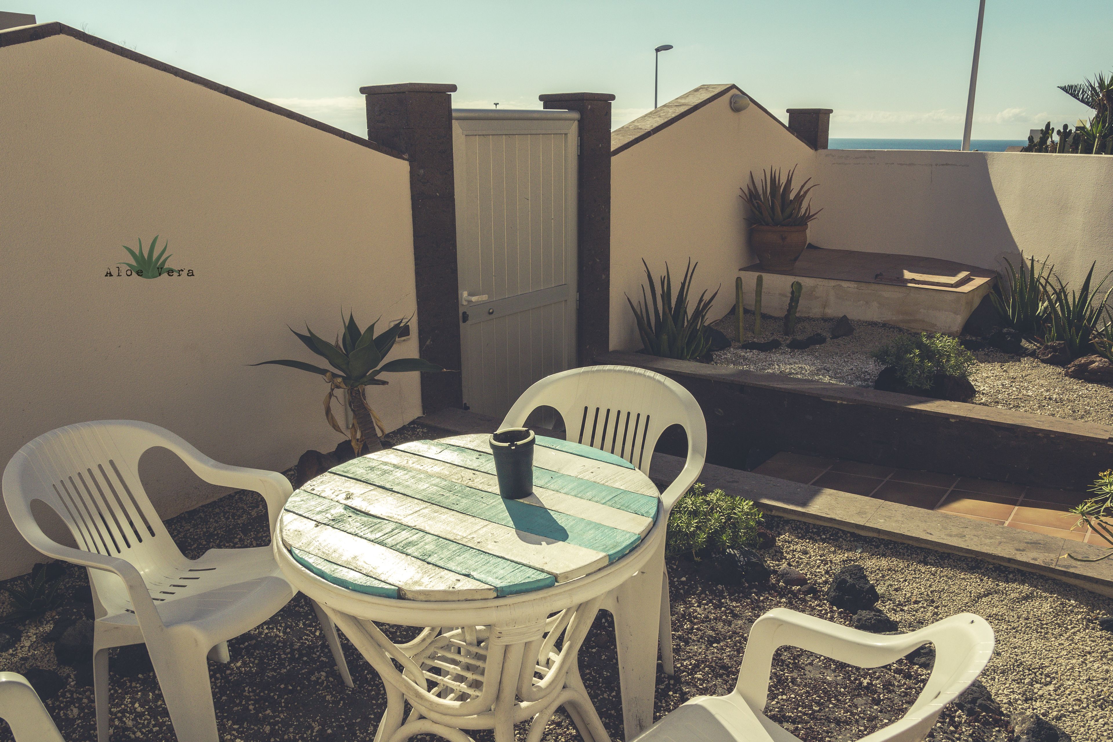 Een terras met een ronde tafel en vier stoelen, een witte deur en potplanten.