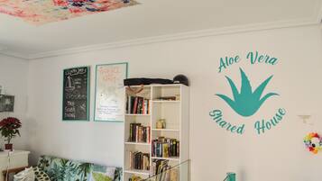 Un salón acogedor con una estantería, un sofá y una pared con la inscripción 'Aloe Vera Shared House'.