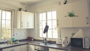 A kitchen with white cabinets, a microwave, a kettle, and a window with a view of greenery. - Aloe Vera Shared House - Hostel (Granadilla de Abona)