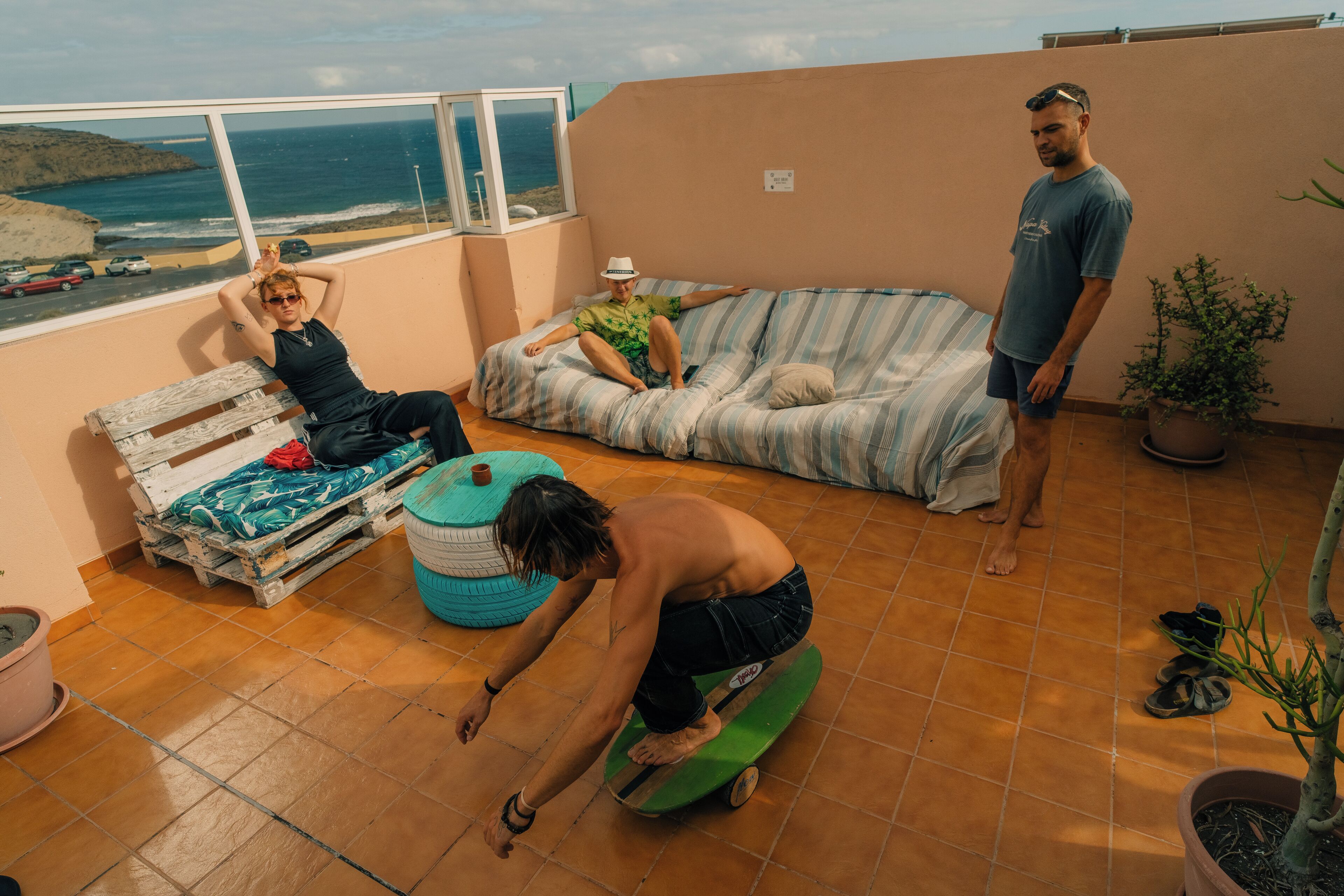 A rooftop terrace with a view of the ocean, a striped sofa, a wooden bench, and a green skateboard.