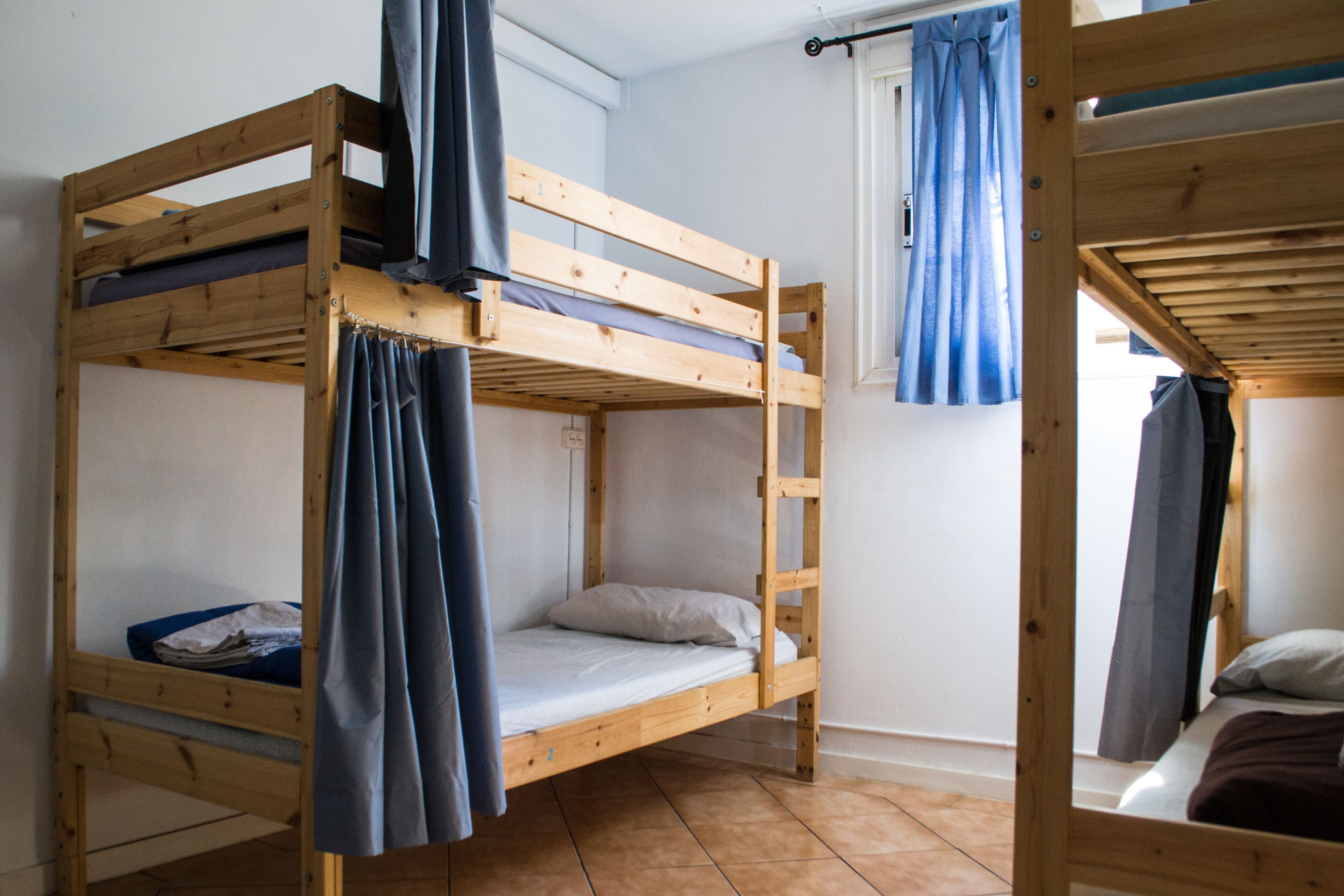 A dormitory-style room with two bunk beds, a window with curtains, and a tiled floor.