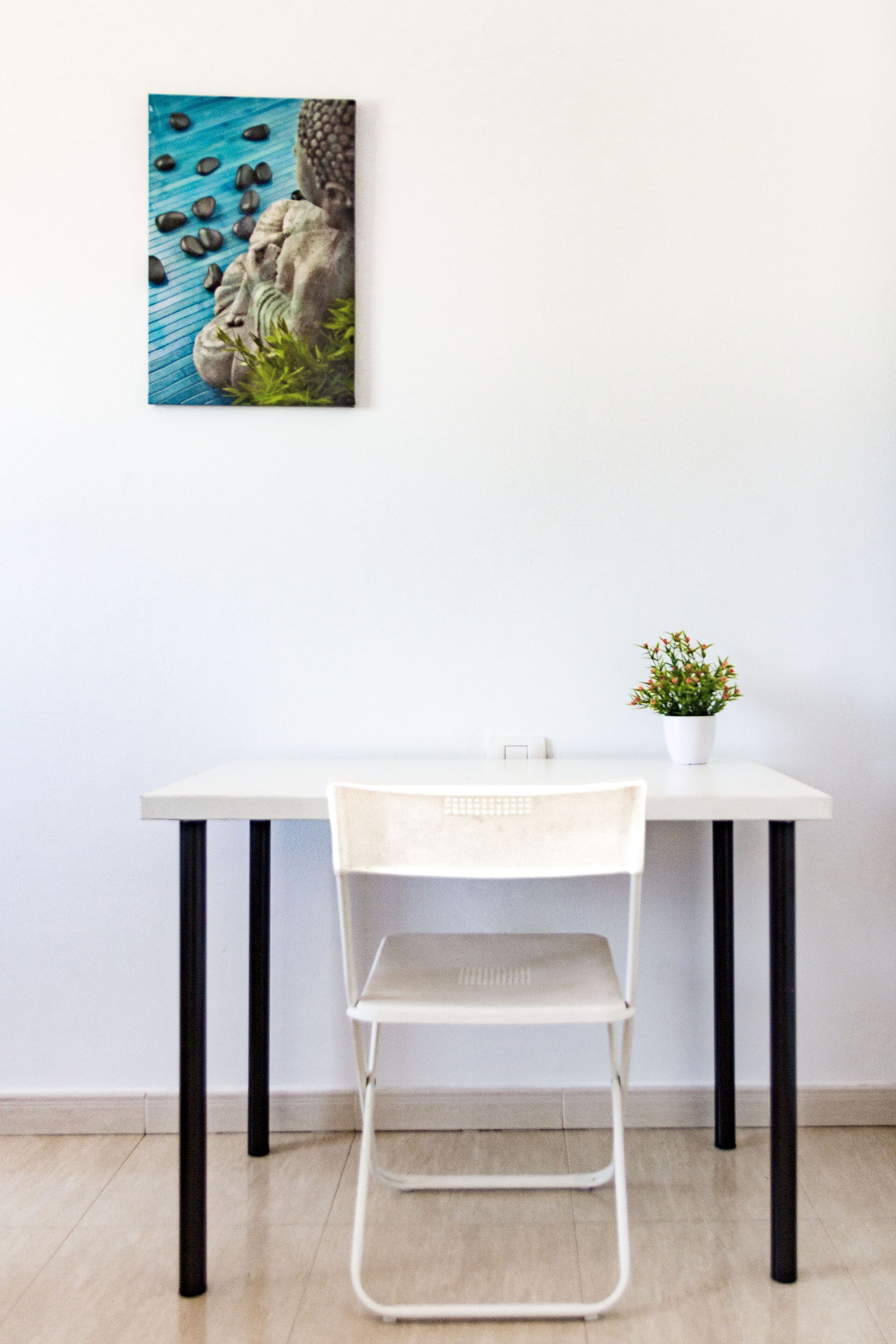 A white table with a white chair, a small potted plant, and a framed artwork on the wall.