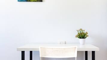 A white table with a white chair, a small potted plant, and a framed artwork on the wall.