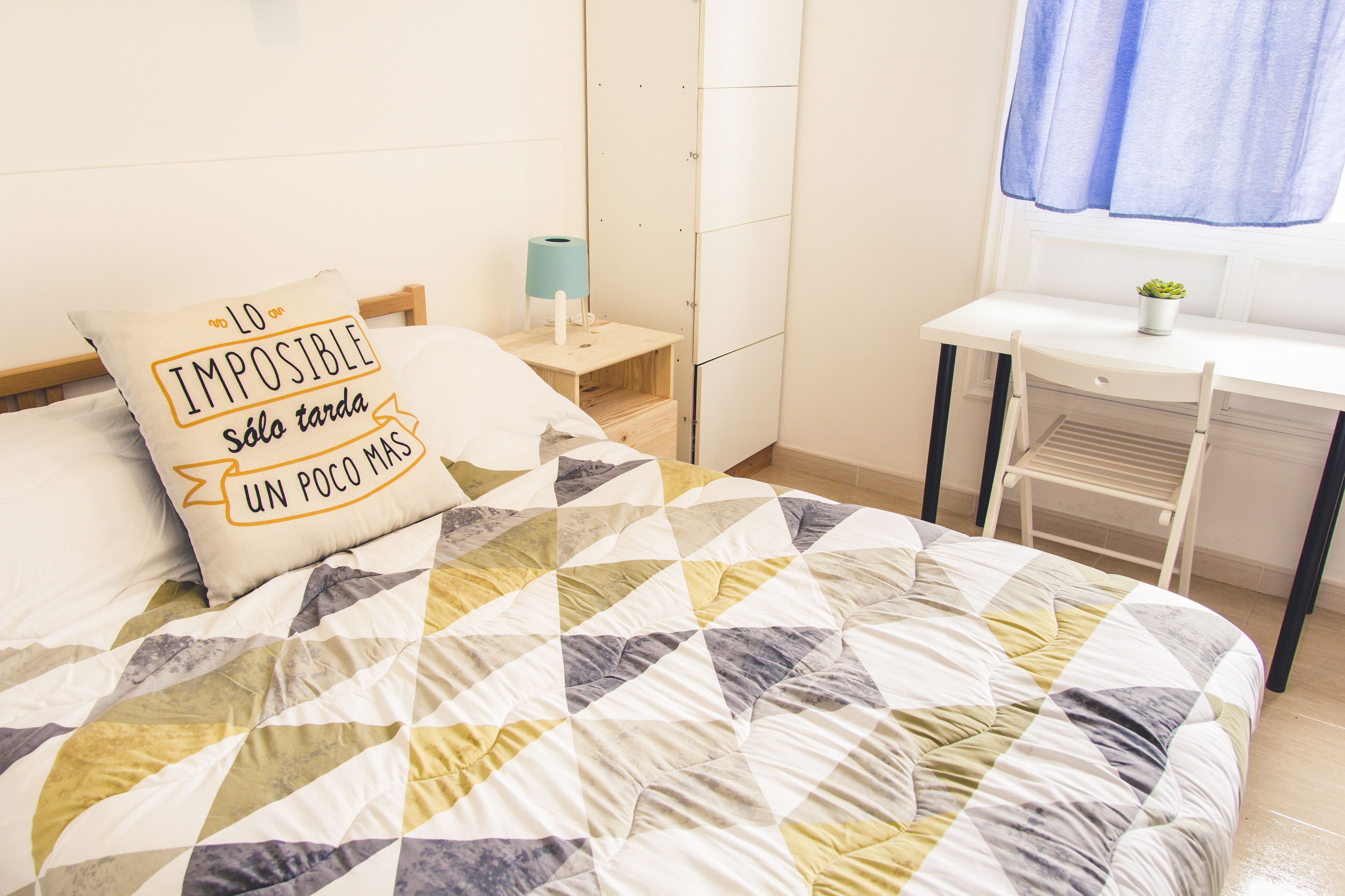 Un dormitorio con cama, escritorio y mesita de noche.